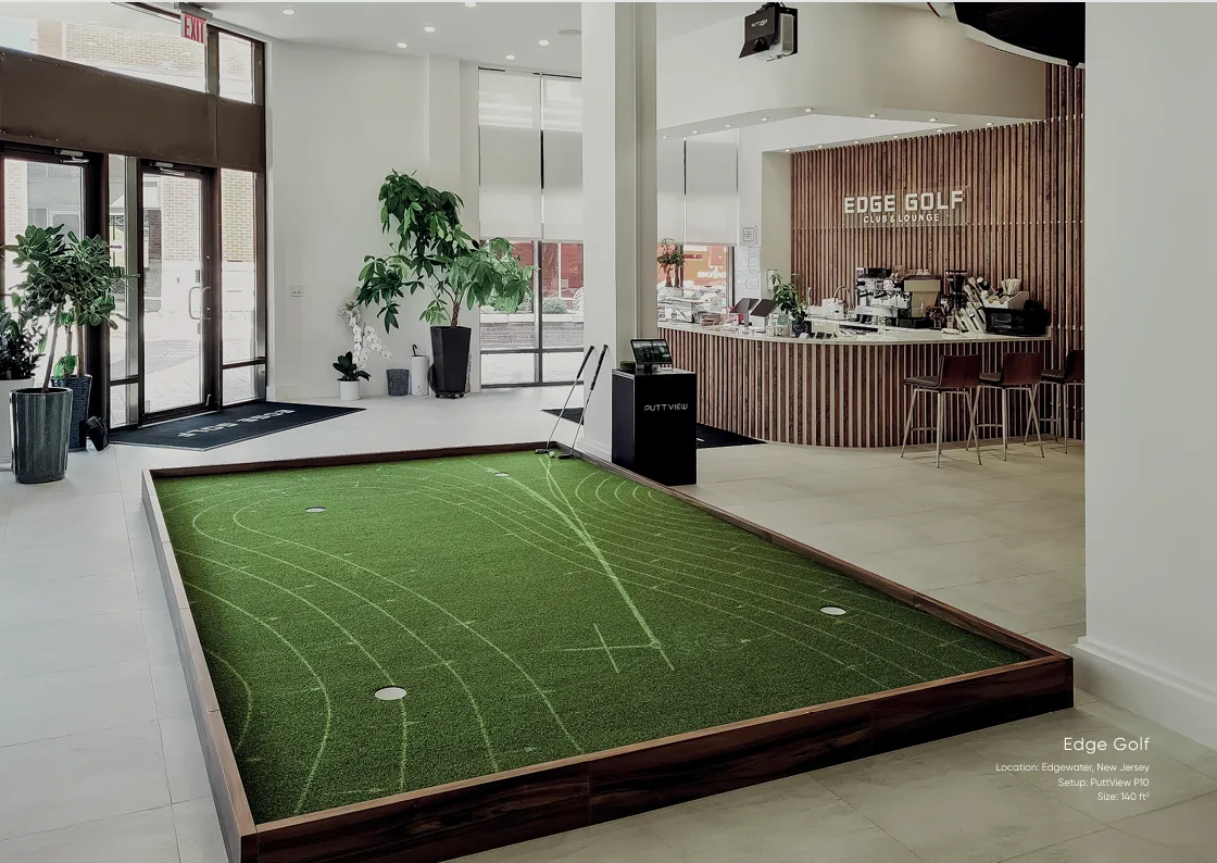 Amplio green de putting interior junto a la recepción luminosa de un club de golf.